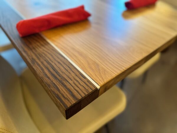 Close-up of South Loft custom wooden dining table with a striped wood grain design and rolled red napkin.