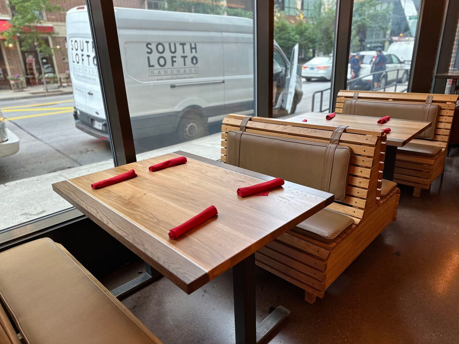 SouthLoft custom wooden booth seating with a rectangular dining table set with red napkins, and a SouthLoft van visible outside.
