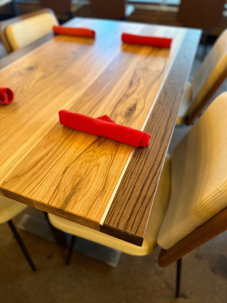 South Loft custom wooden restaurant tables with a striped wood grain design, set with rolled red napkins.