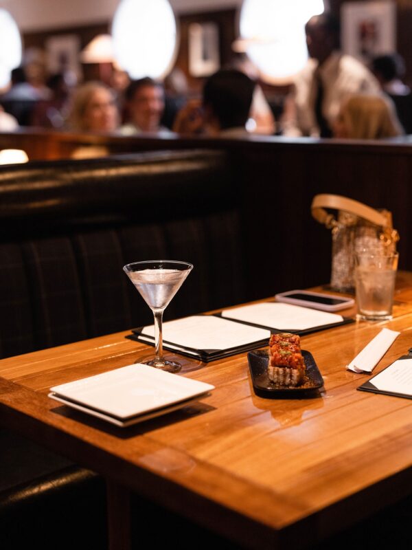South Loft custom wooden table with sushi, a cocktail, and menus in a lively dining booth setting.