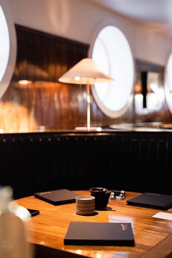 South Loft custom wooden table with menus and tableware in a booth, lit by a lamp in a nautical-themed dining area.