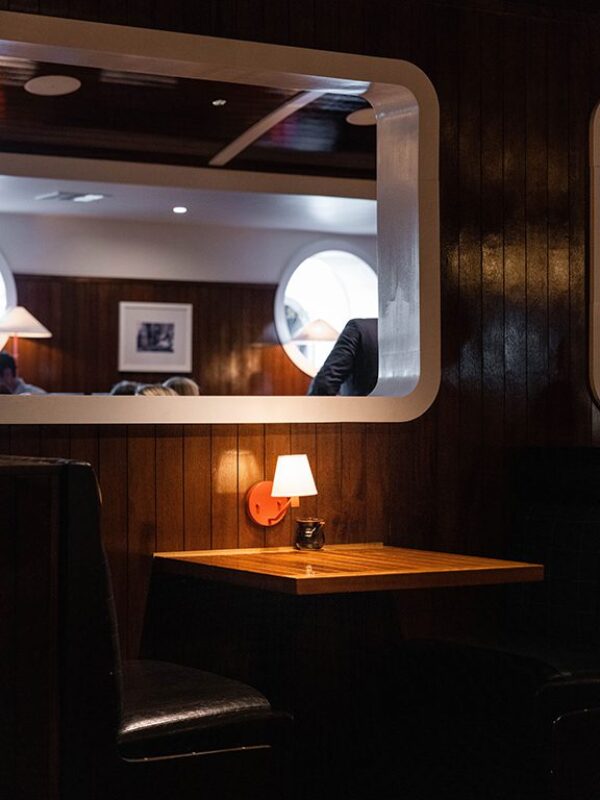 South Loft custom wooden table with a wall-mounted lamp in a cozy booth setting with a view into the next room.