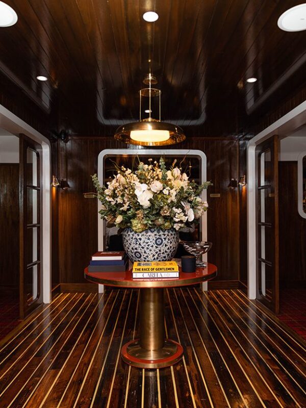 South Loft custom round pedestal table with a floral arrangement and decor in a luxurious wooden hallway.