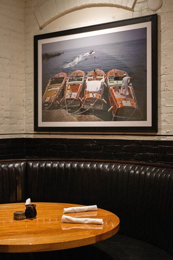 South Loft custom round wooden dining table in a black leather booth beneath framed boat artwork.