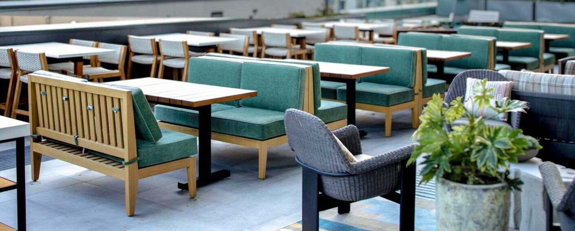 A row of SouthLoft made hardwood table tops and metal 205 Series bases are on the outdoor seating are of a restaurant.