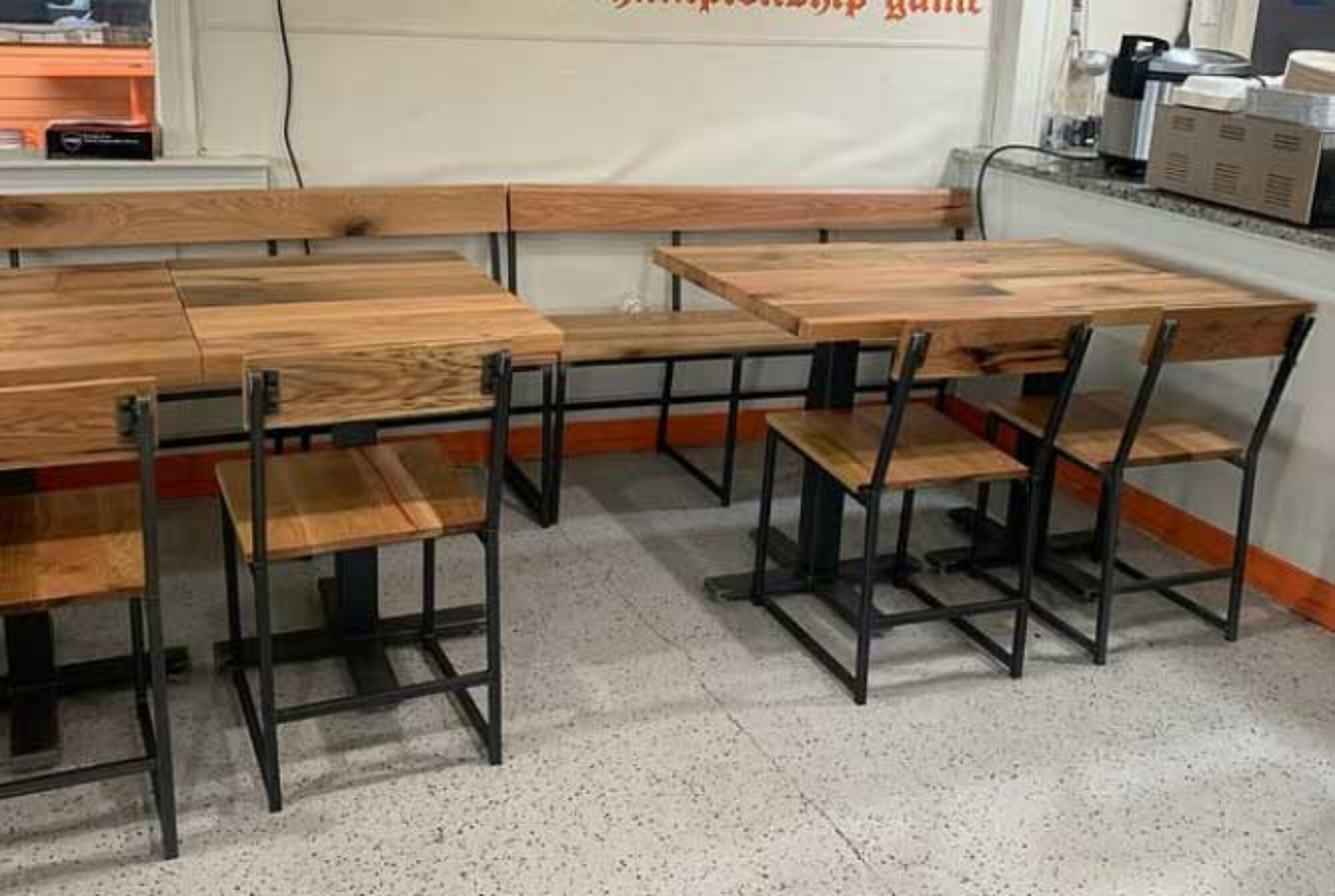 A pair of hardwood tables sits inside of a restaurant. 300 Series seating from SouthLoft and wooden bench seating are adorning the tabletop.