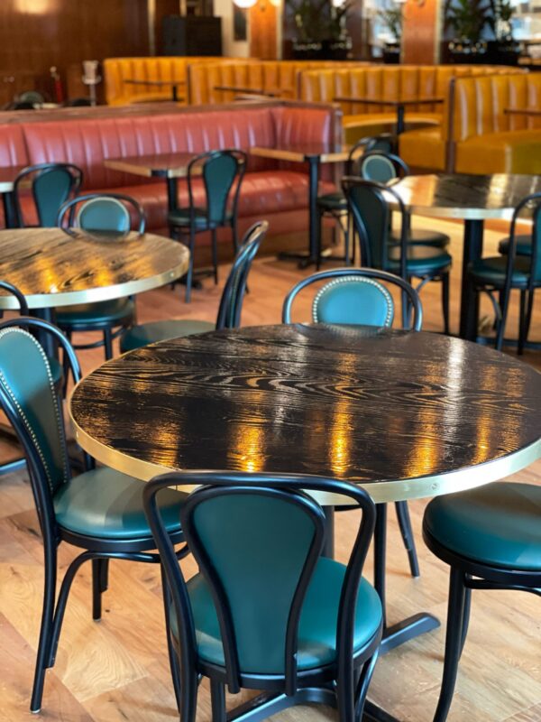 A group of round SouthLoft built tabletops with metallic details sit inside Goodwins Dallas location.