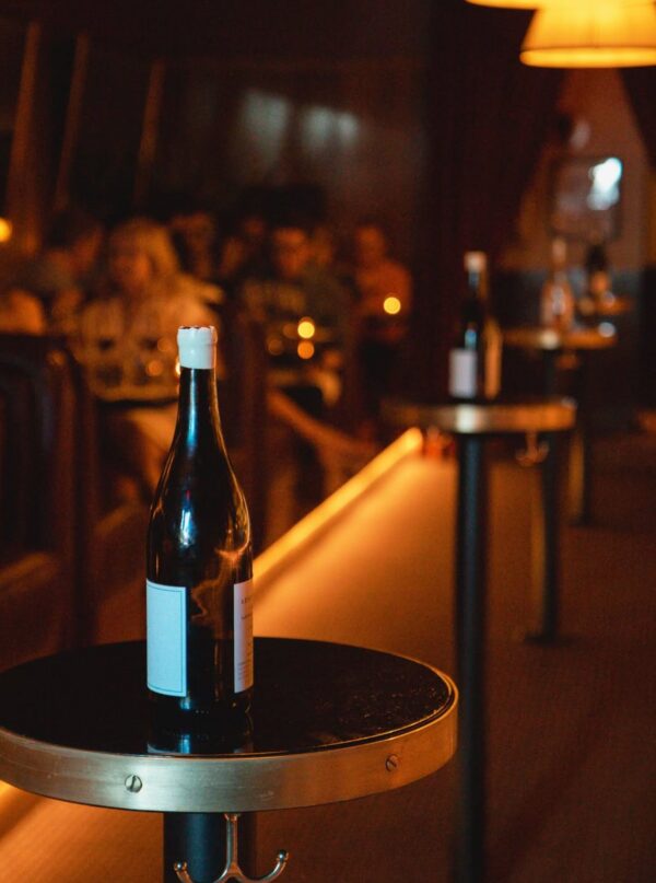 A bottle of wine sits on a small standing height table built by SouthLoft. This table has a ebony finish and metallic accents.